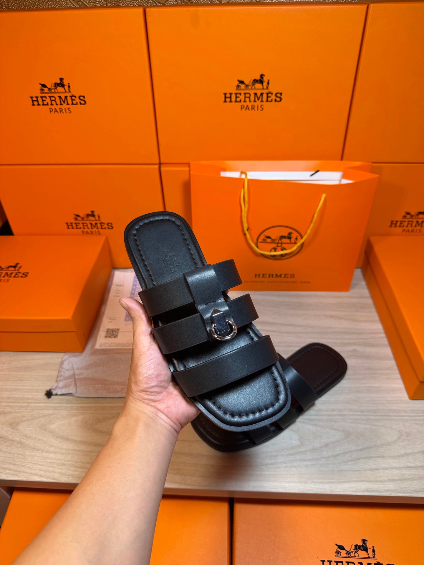 Hand holding dark leather Hermes slide sandal with two straps and metal buckle
