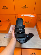 Dark leather Hermes slide sandal held up, showing two straps and metal buckle