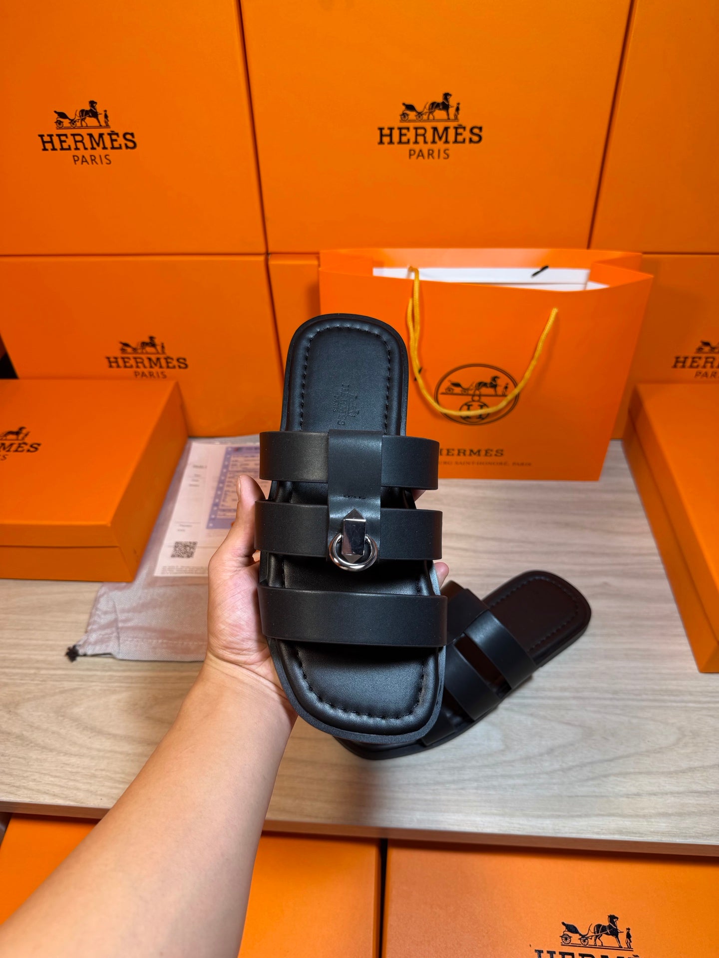 Dark leather Hermes slide sandal held up, showing two straps and metal buckle