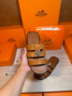 Brown leather sandals in hand, tan footbed with two straps and silver buckle.