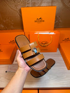 Brown leather sandals in hand, showing two straps and silver buckle hardware.