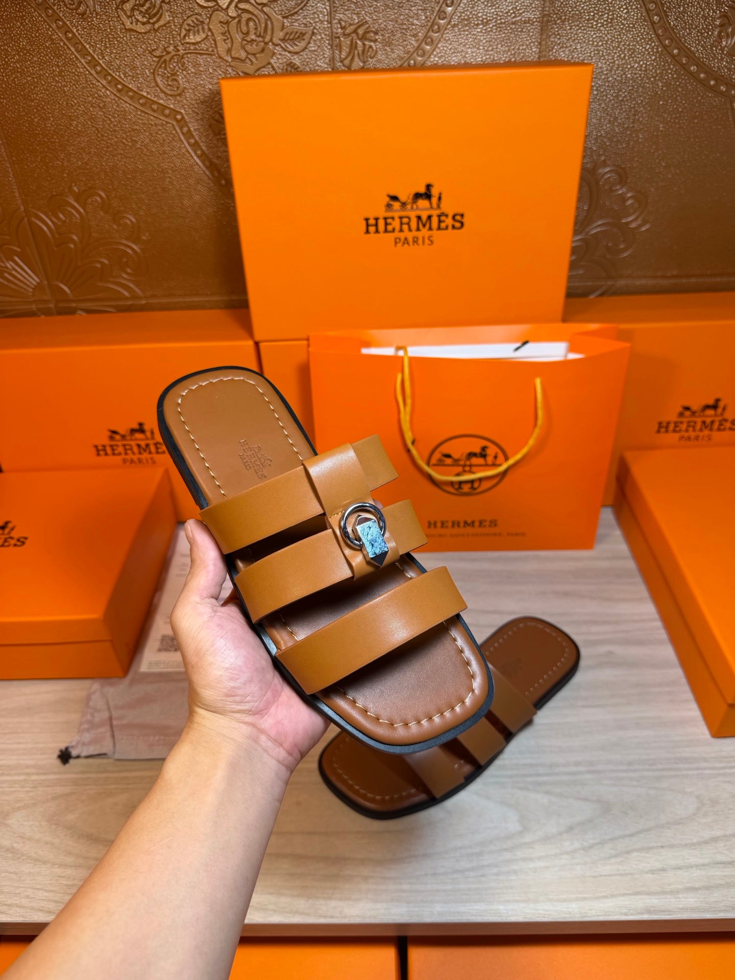 Brown leather sandals in hand, showing two straps and silver buckle hardware.