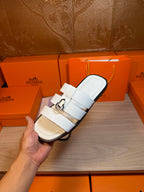 Hermes white leather slide sandal held in hand, front strap detail and silver buckle