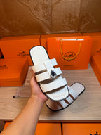 Hermes white leather slide sandal held in hand, double straps and silver buckle