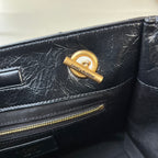 Black leather tote bag with gold YSL logo charm on front panel