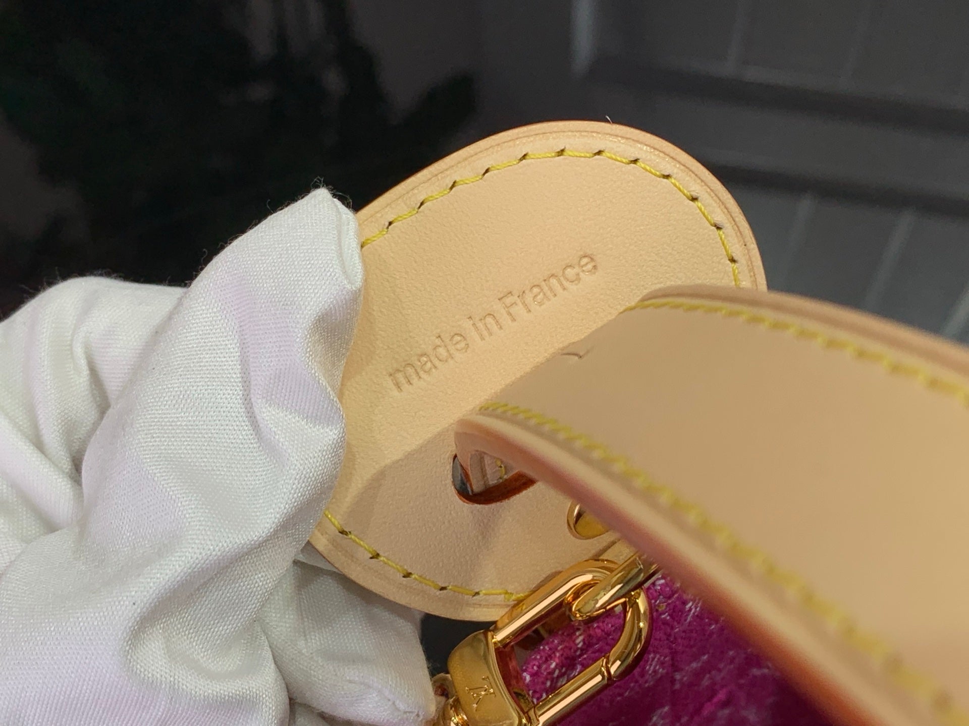 Gold-tone clasp and tan leather base with stitching on magenta monogram bag