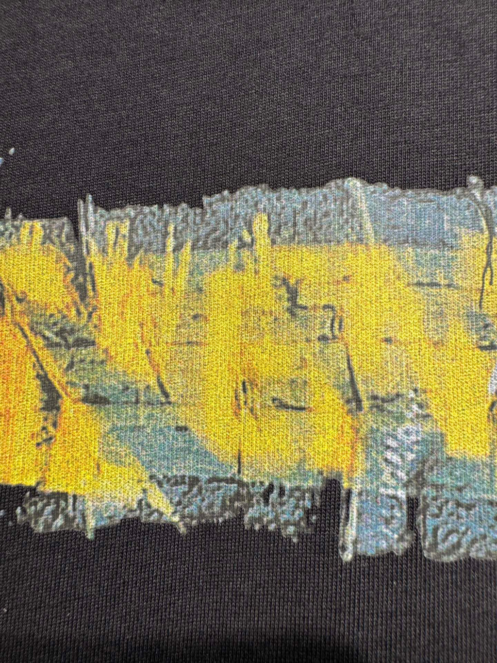 Black crewneck T-shirt close-up showing yellow and blue paint-style graphic print