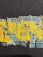 Black crewneck T-shirt close-up showing yellow and blue paint-style graphic print