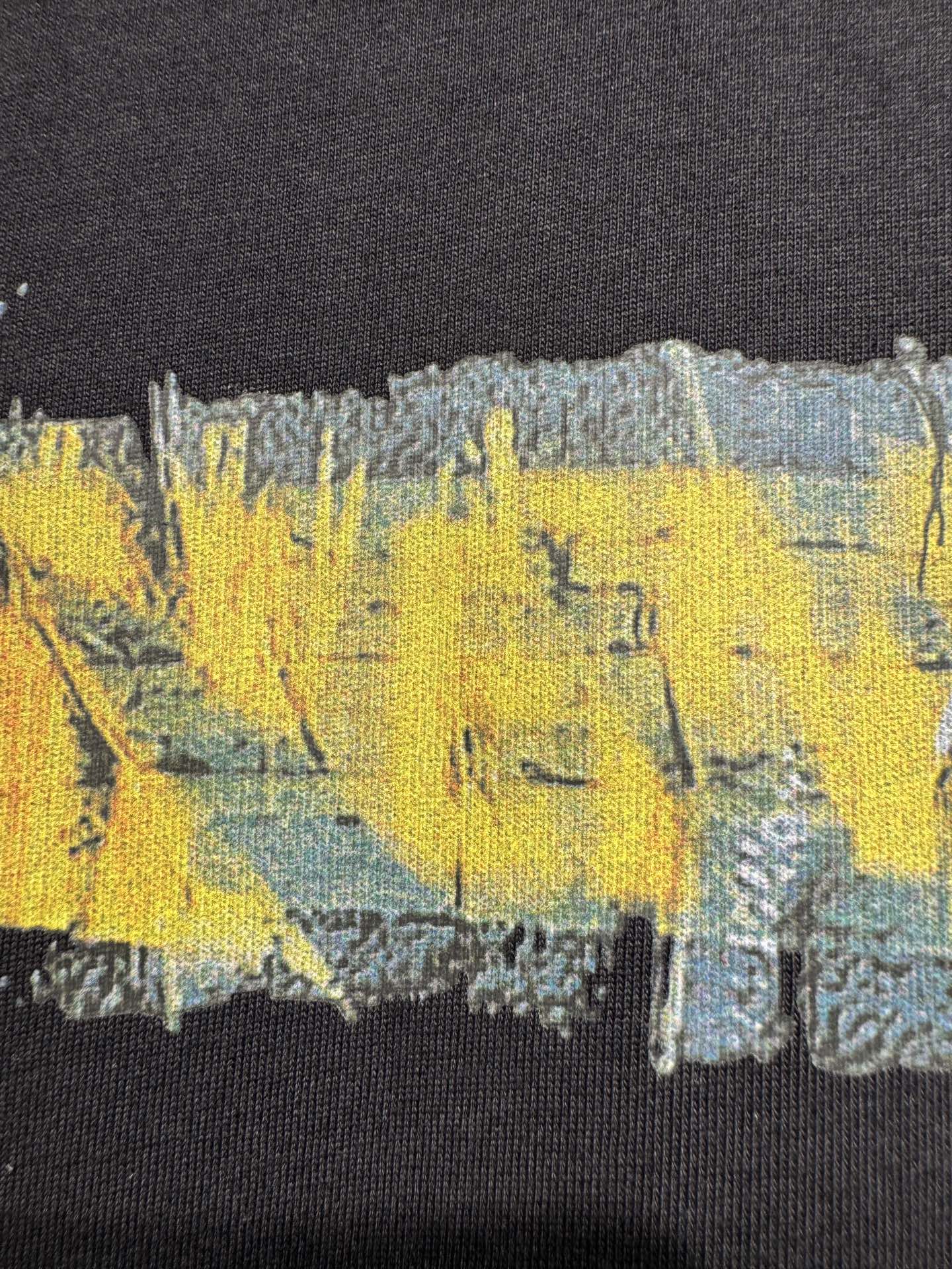 Black crewneck T-shirt close-up showing yellow and blue paint-style graphic print