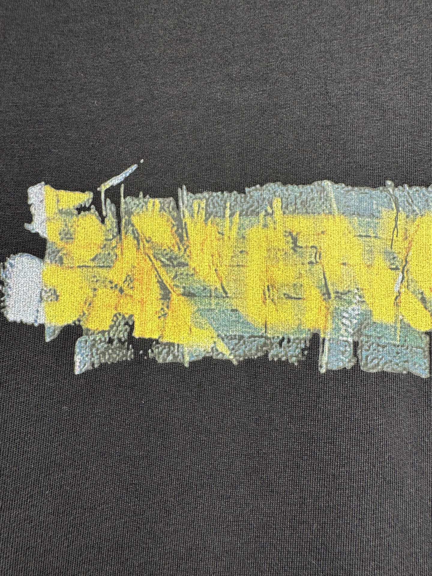 Black crewneck T-shirt with close-up yellow, blue, and aqua paint-style graphic print
