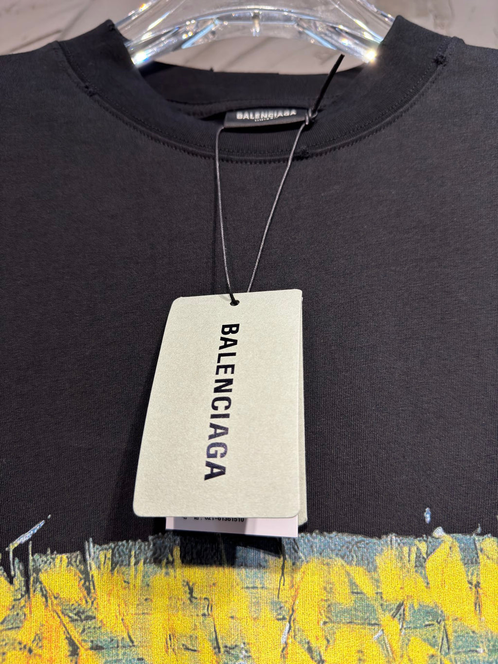 Black crewneck T-shirt on hanger with Balenciaga size tag and yellow graphic