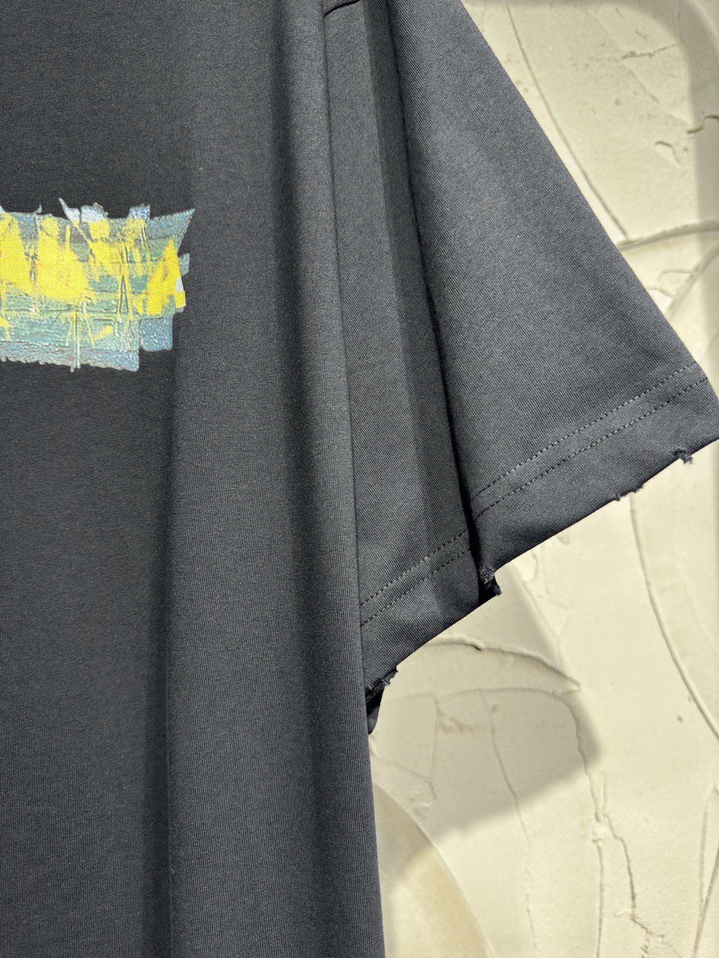 Black crewneck T-shirt with visible short sleeve hem and partial yellow graphic