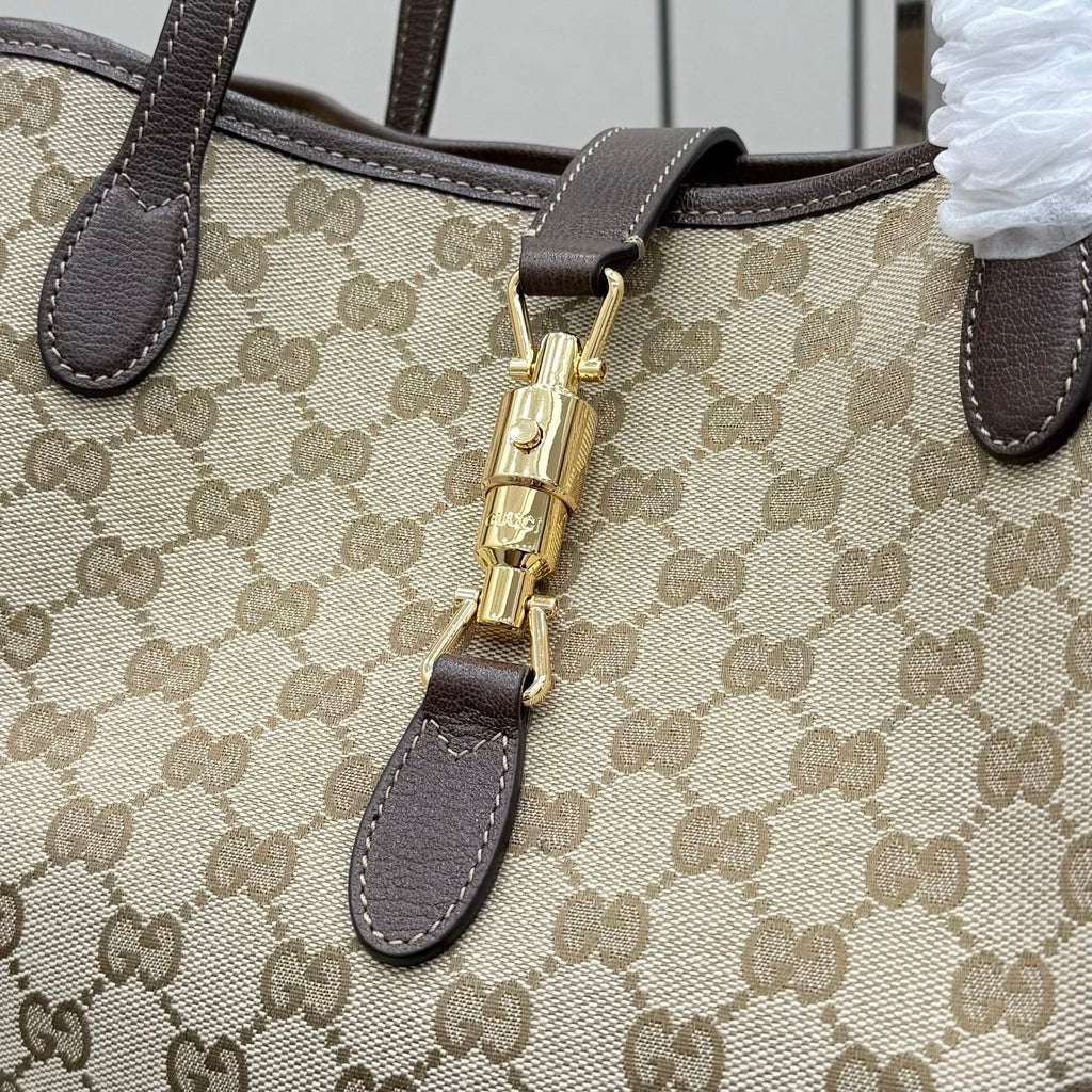 Gucci GG canvas tote bag close-up of gold zip pull and dark leather trim