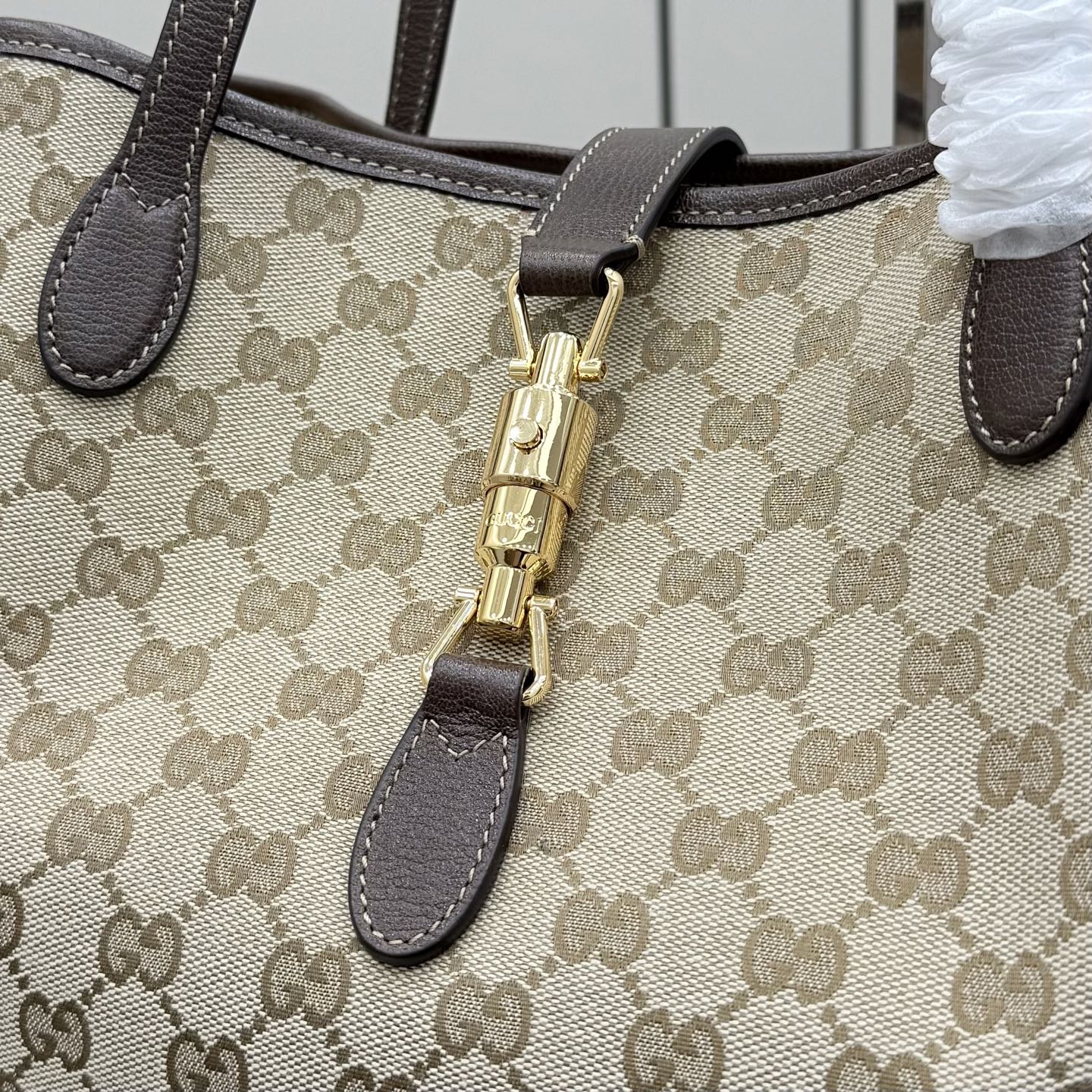 Gucci GG canvas tote bag close-up of gold zip pull and dark leather trim
