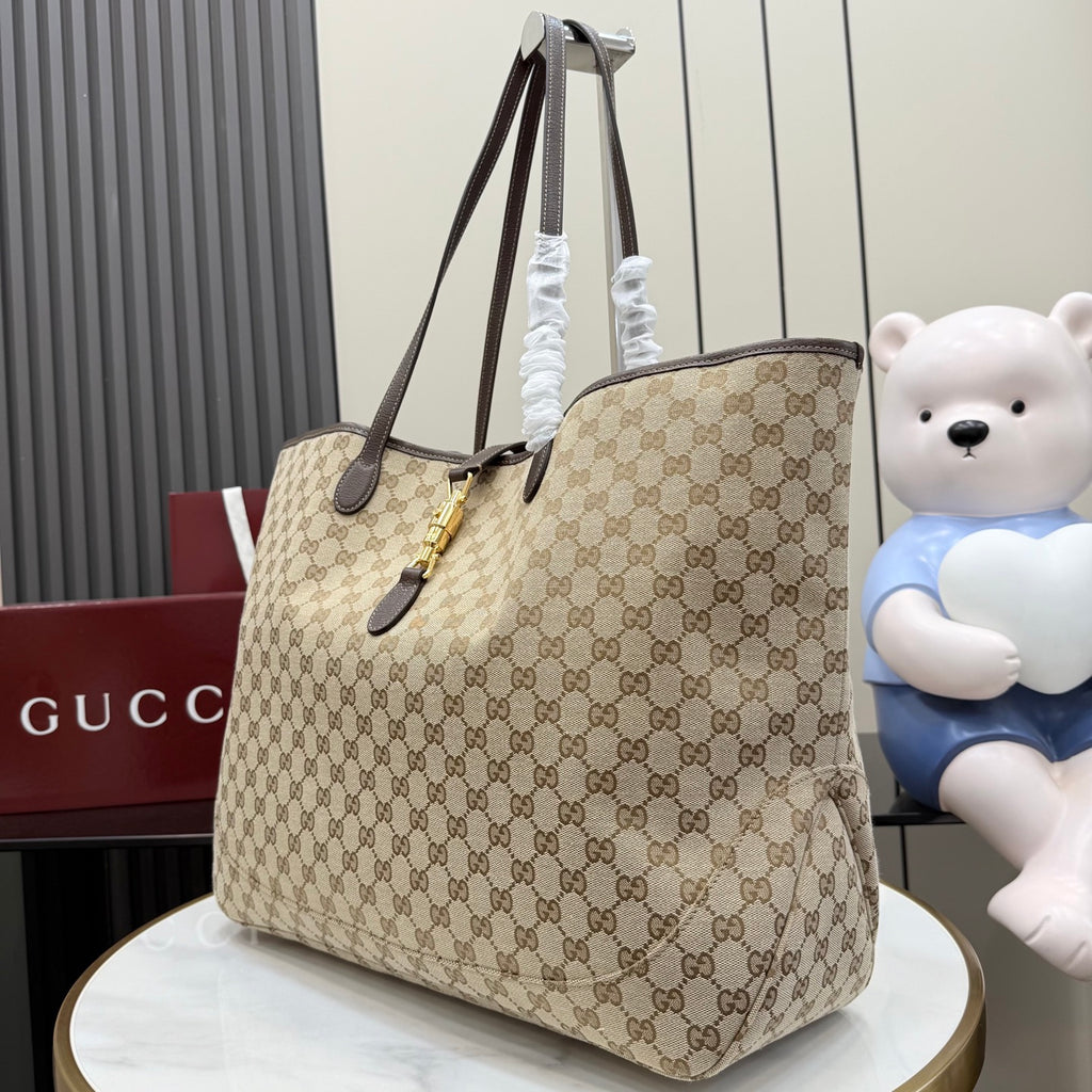 Gucci GG canvas tote bag with dark leather handles and gold hardware, angled view