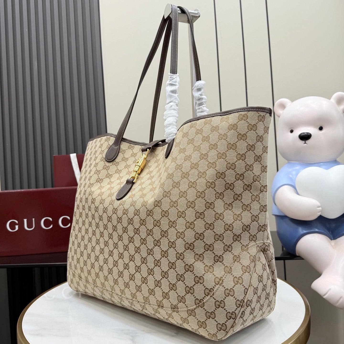 Gucci GG canvas tote bag with dark leather handles and gold hardware, angled view