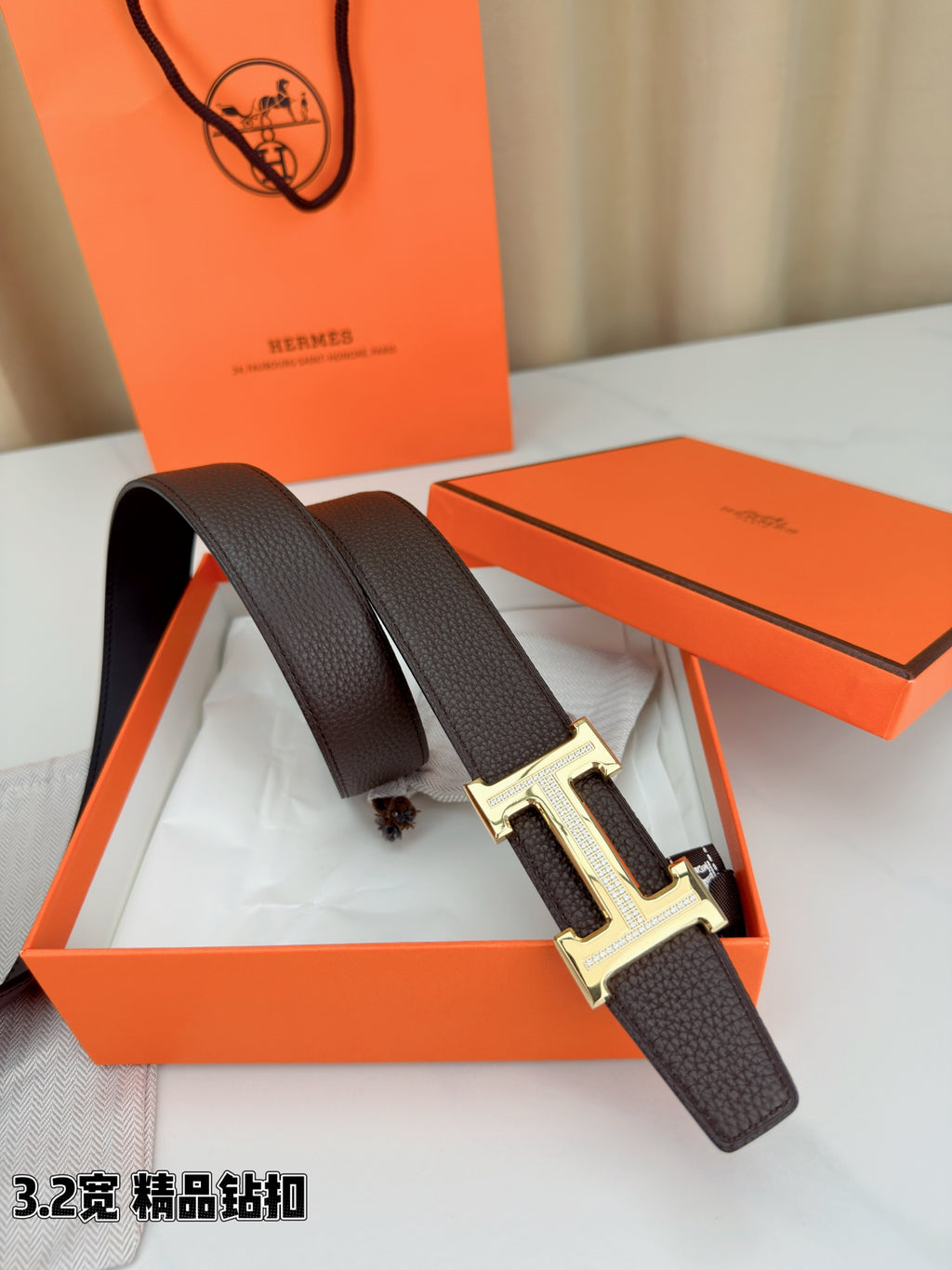 Dark brown leather belt with H buckle, shown near open orange box