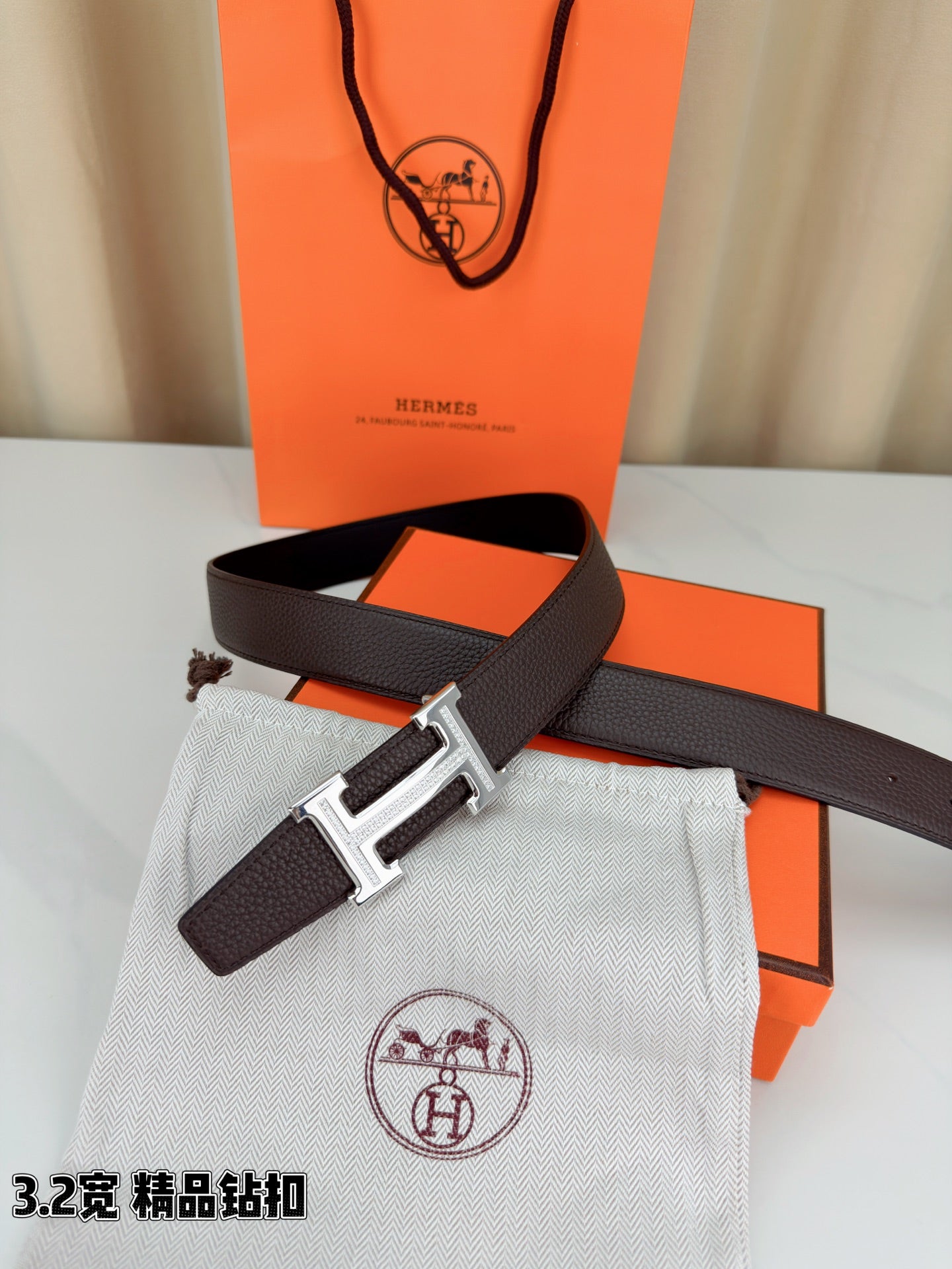 Dark brown leather belt with H buckle on fabric pouch beside orange box