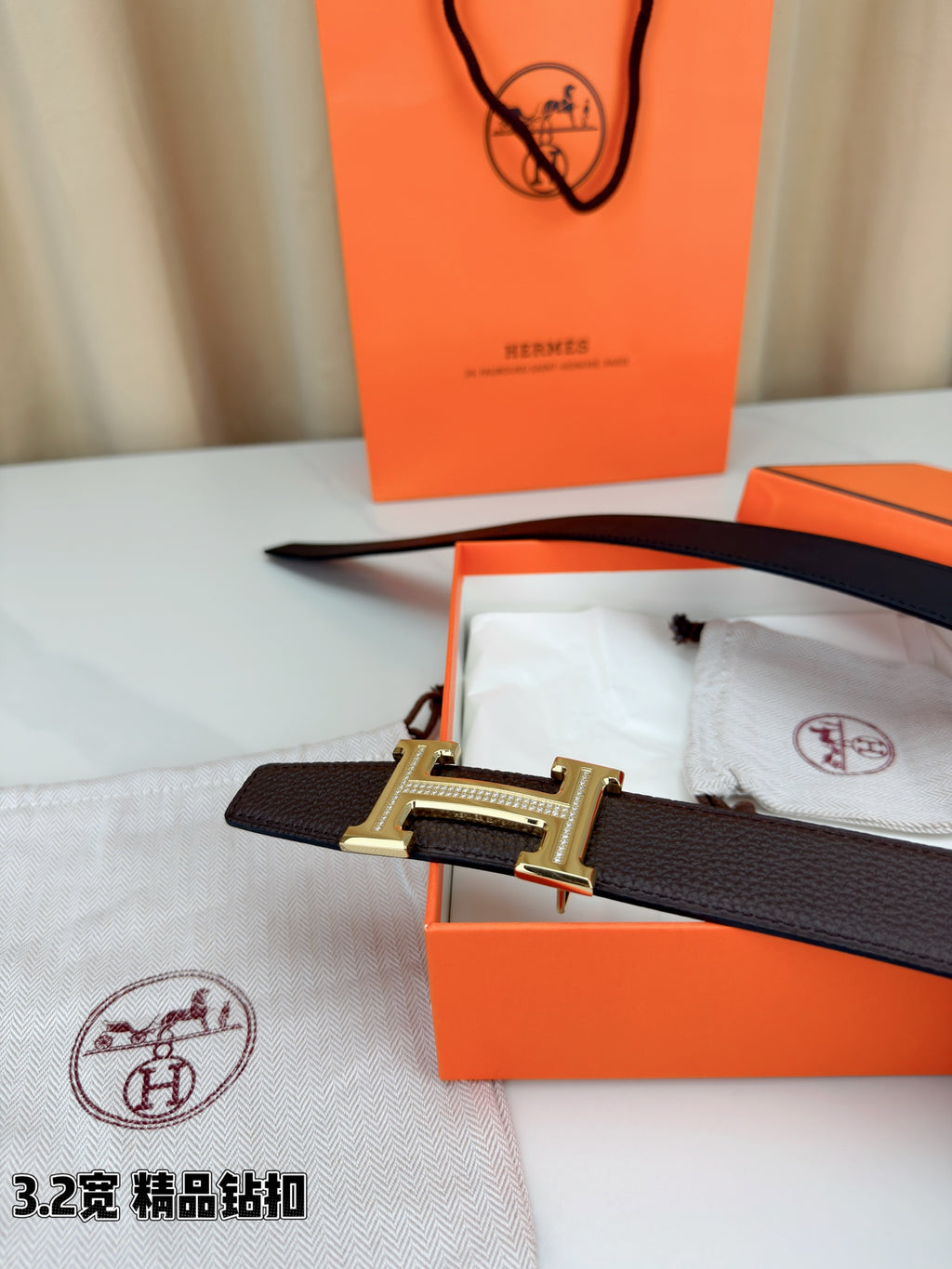 Dark brown leather belt with H buckle on dust bag, with orange box nearby