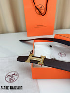 Dark brown leather belt with H buckle on dust bag, with orange box nearby