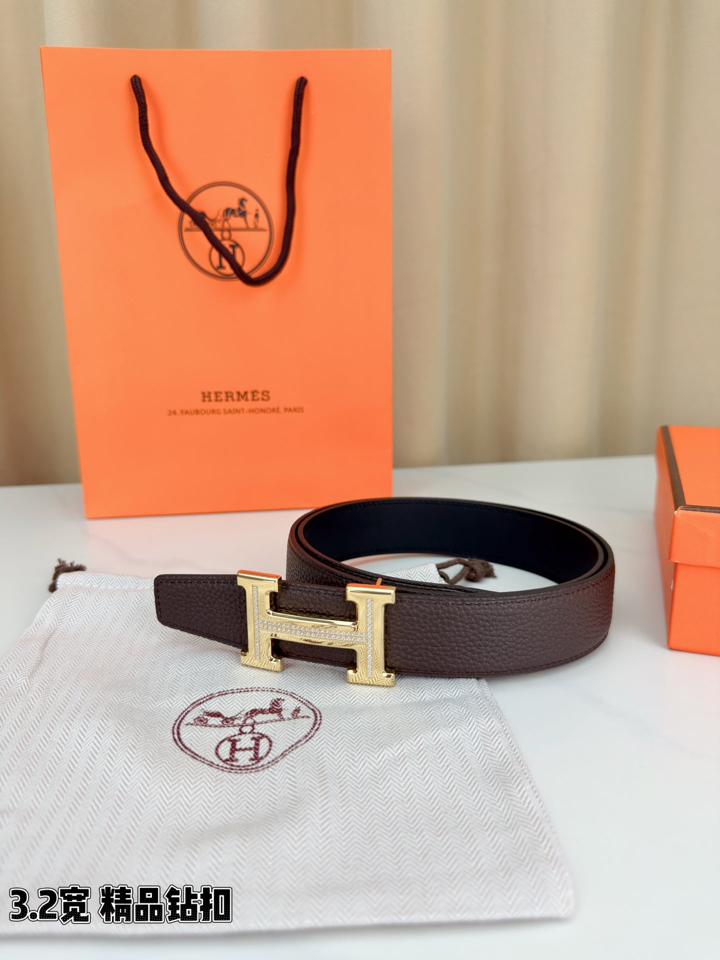 Dark brown leather belt with H buckle resting on dust bag beside box