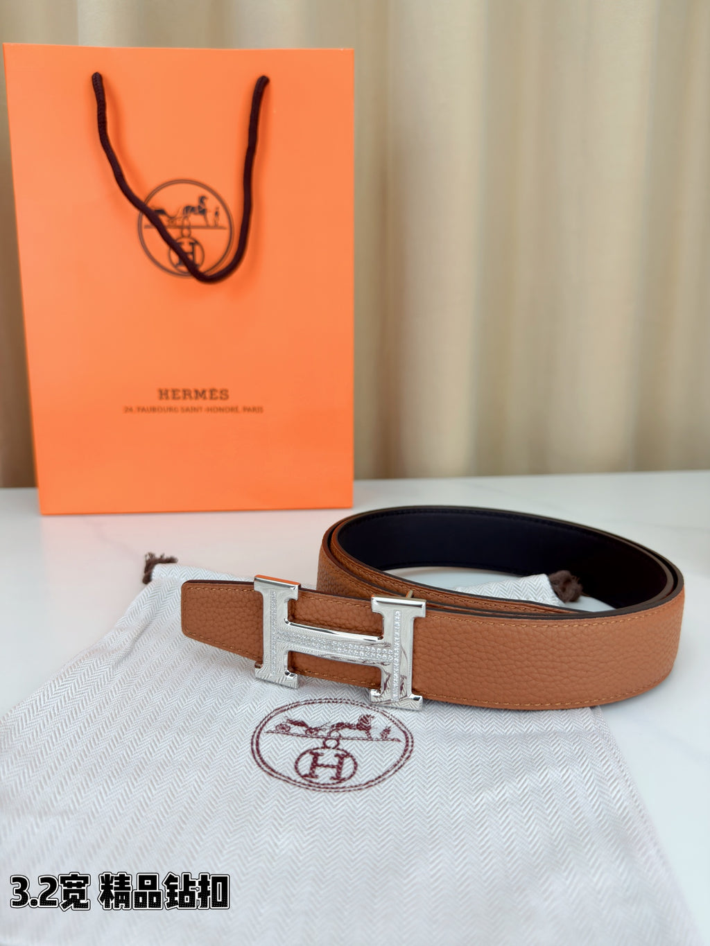 Tan leather belt with black interior and silver H buckle on fabric pouch