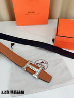 Leather belt with tan strap and silver H buckle laid on textured cloth