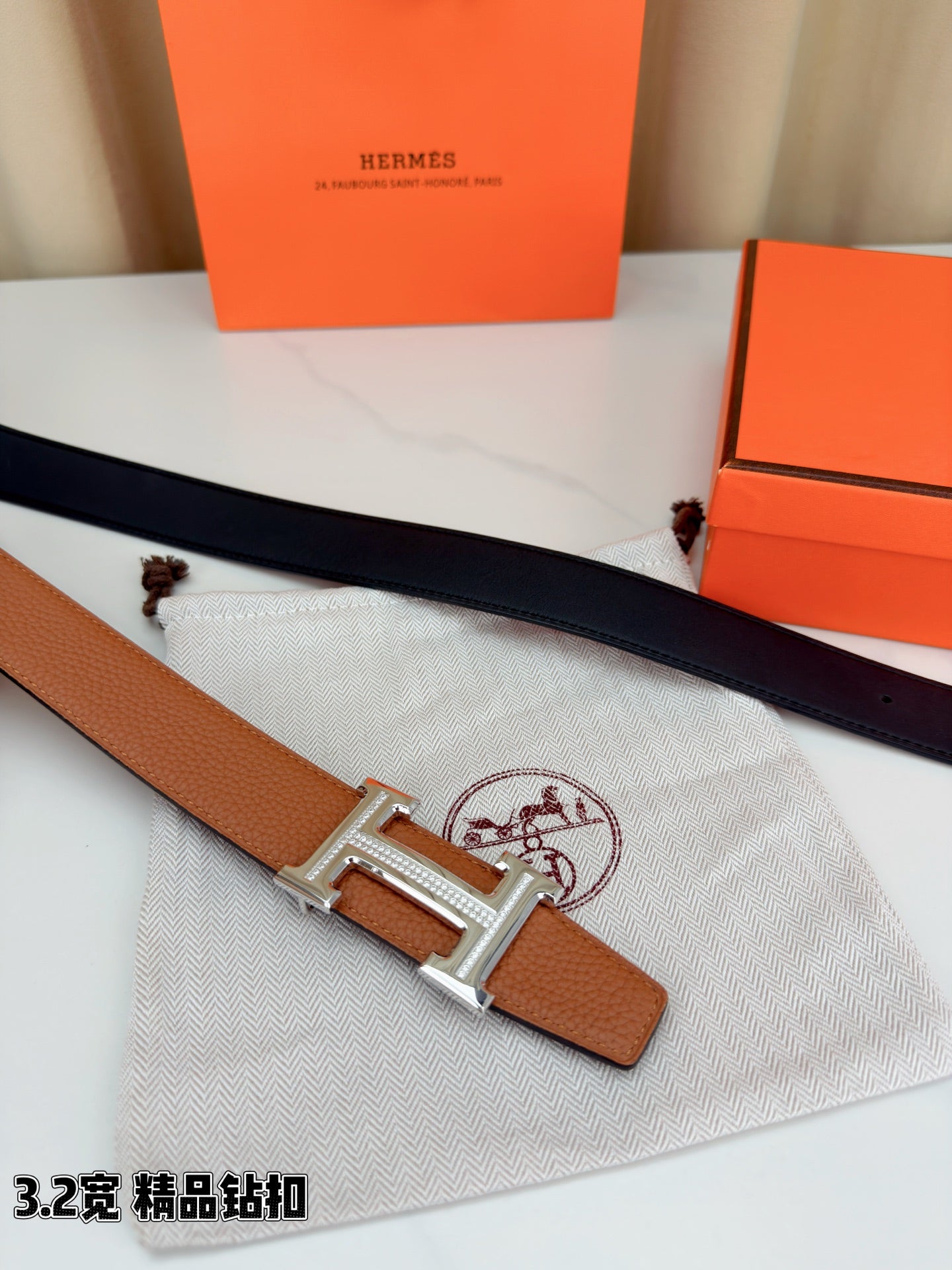 Leather belt with tan strap and silver H buckle laid on textured cloth