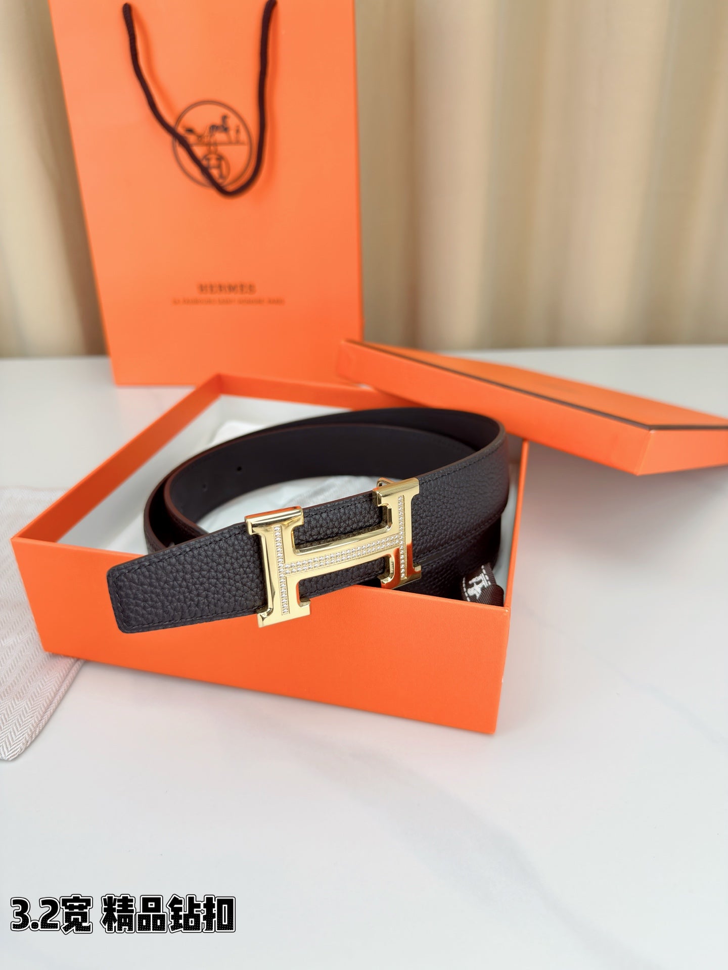 Hermes belt on orange box: dark textured strap with gold-tone H buckle