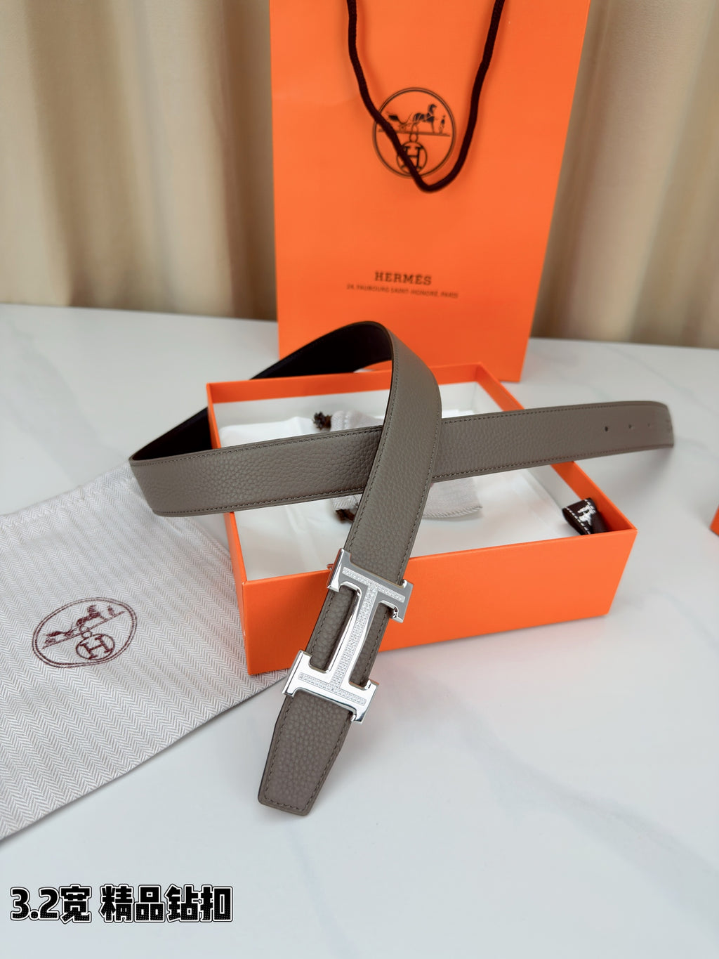 Light gray Hermes belt with silver-tone buckle and long strap laid across box