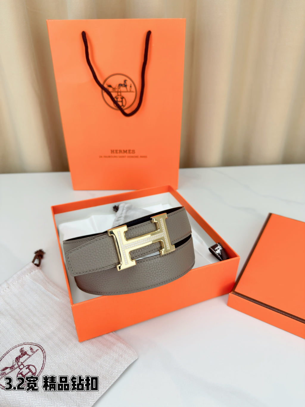 Light gray Hermes belt with gold-tone H buckle, displayed in open gift box