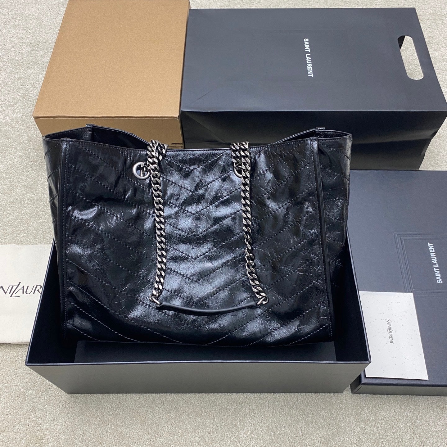 Quilted black tote bag with chain handles and YSL logo at the center