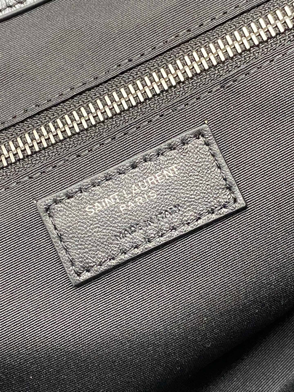 Logo patch on black leather bag near zipper with metallic teeth trim