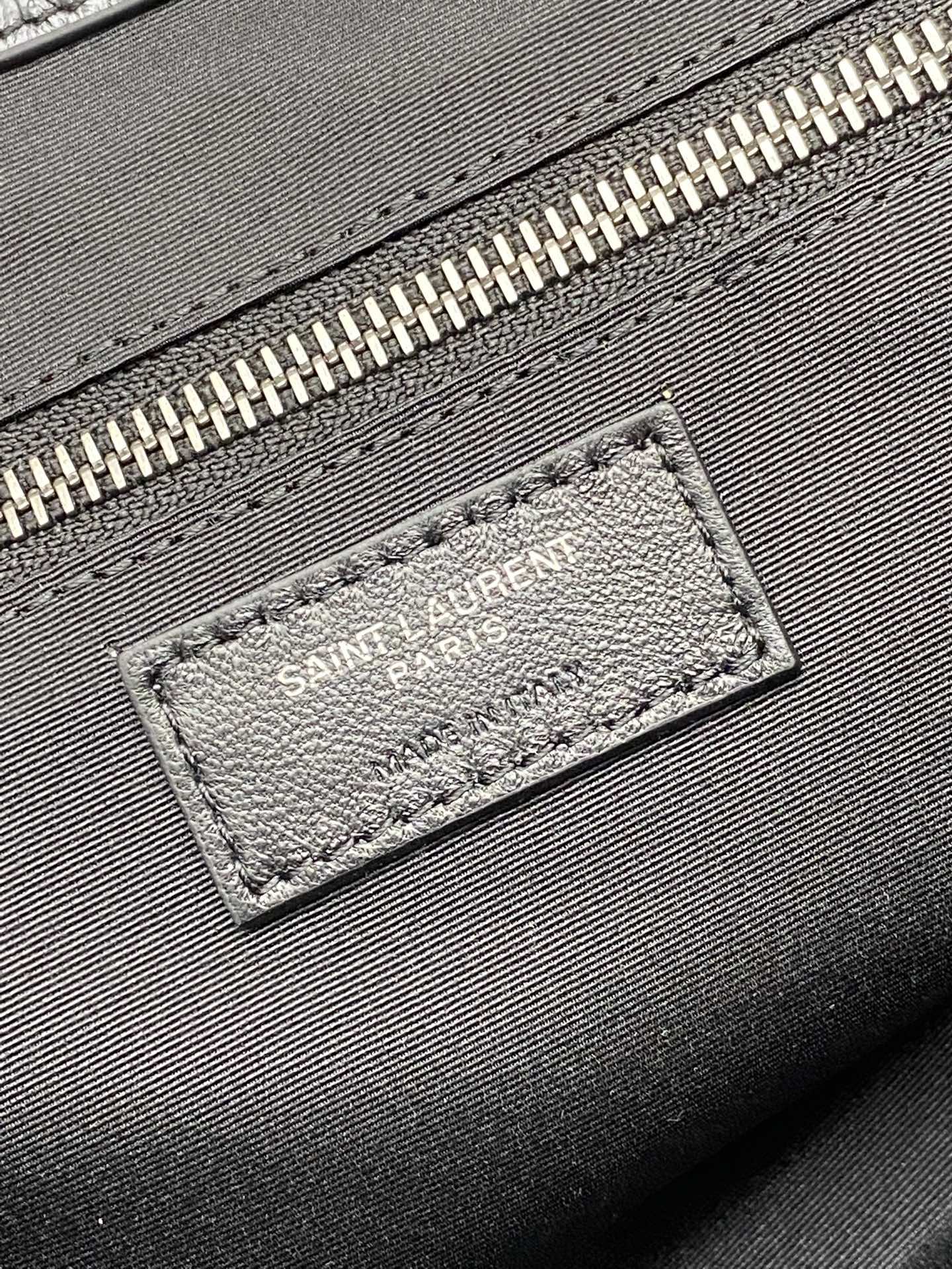 Logo patch on black leather bag near zipper with metallic teeth trim