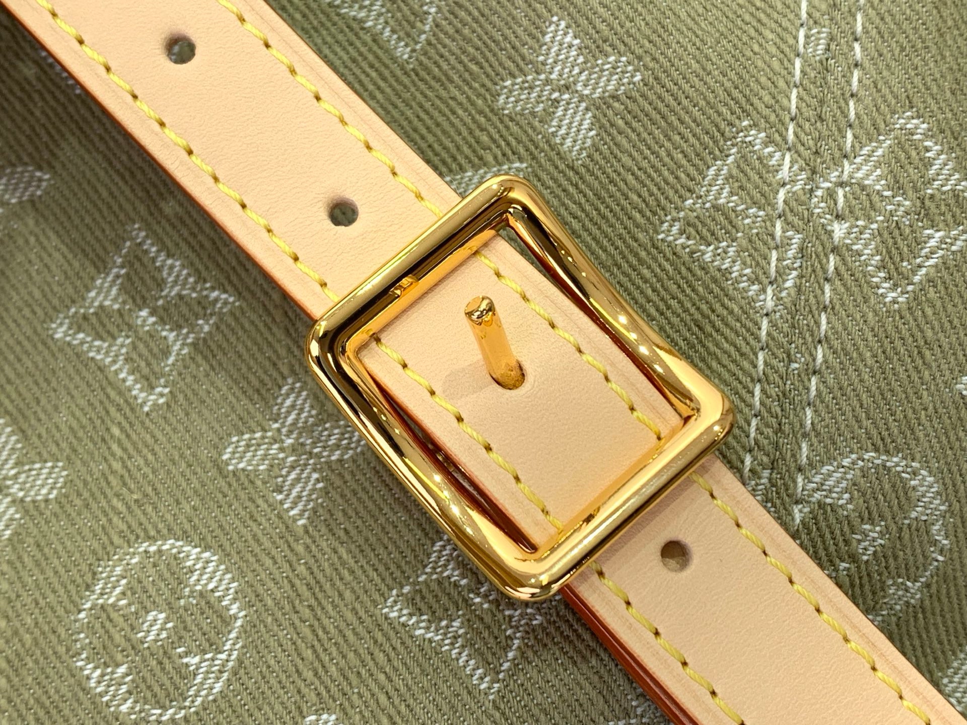 Gold-tone buckle on tan leather strap with eyelets and stitched detail