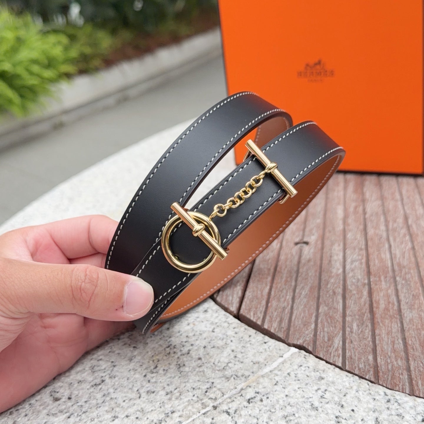 Hermes belt close-up with gold buckle, chain charm, and tan underside