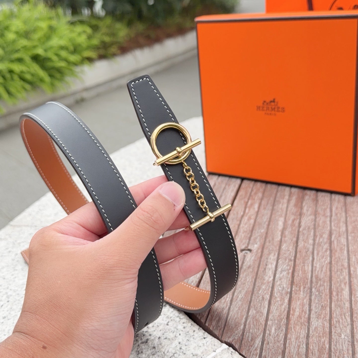 Hermes belt shown by hand, dark navy strap with gold buckle and tan lining