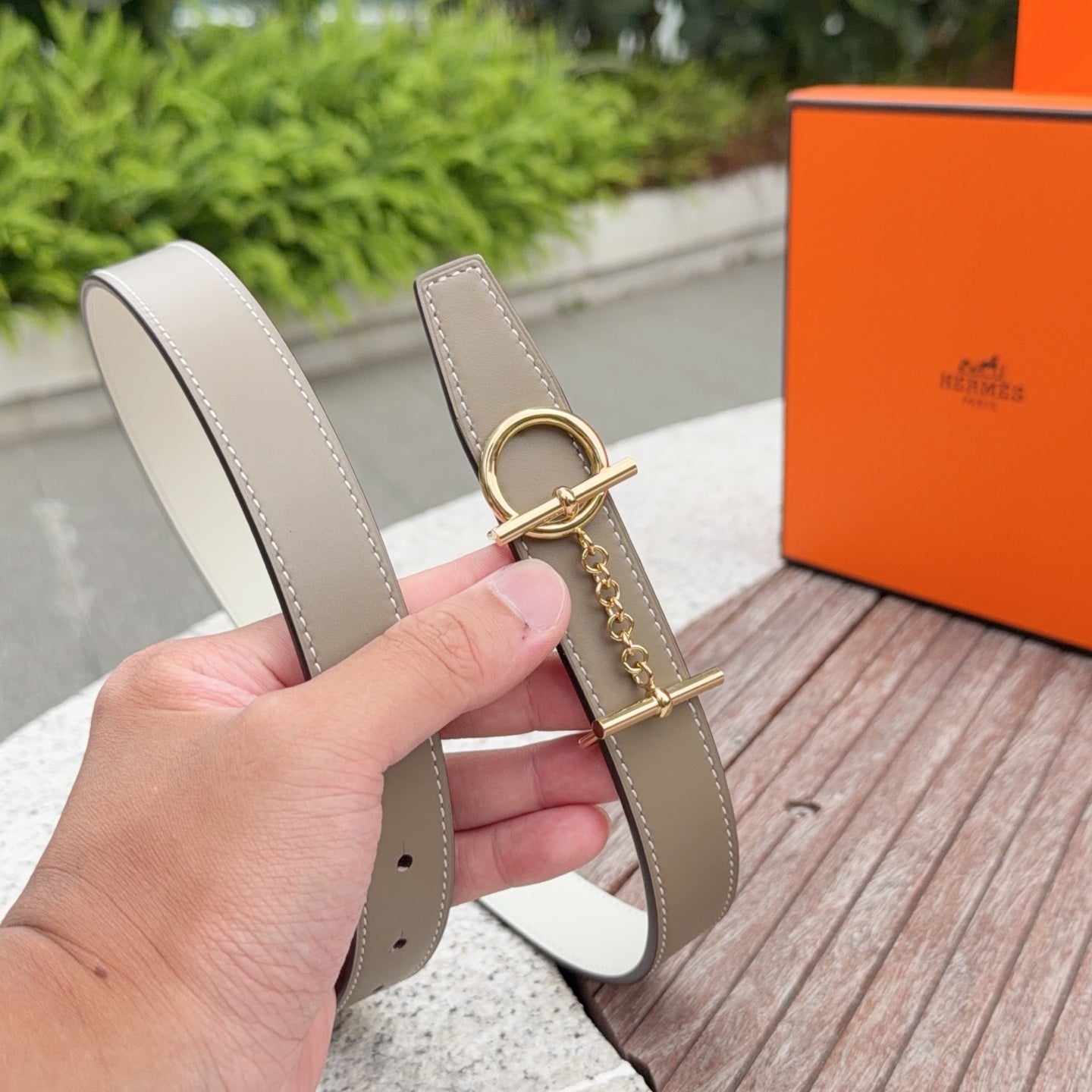 Hermes belt taupe leather strap with gold buckle, held in hand