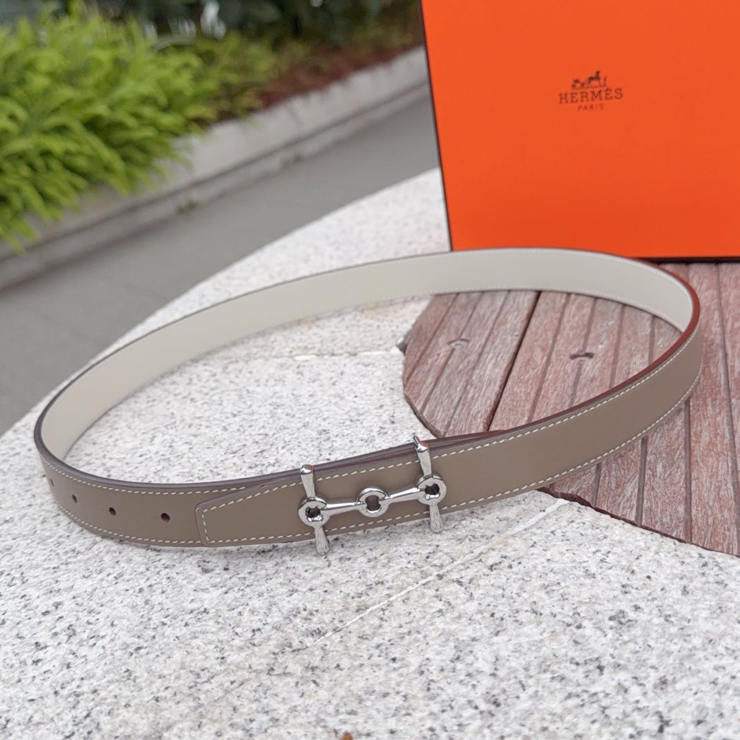 Hermes belt with light tan leather strap and silver buckle hardware on a desk