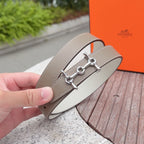 Hermes belt with light tan leather strap and silver buckle clasp, handheld close-up