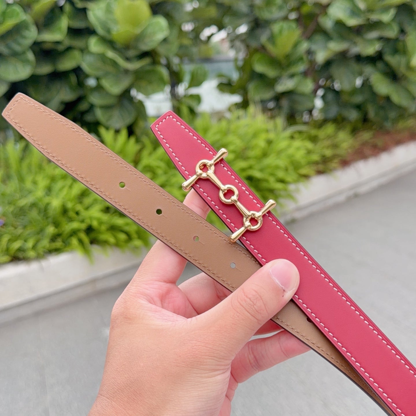 Hermes belt detail, red strap with tan underside and gold-tone double-ring clasp.