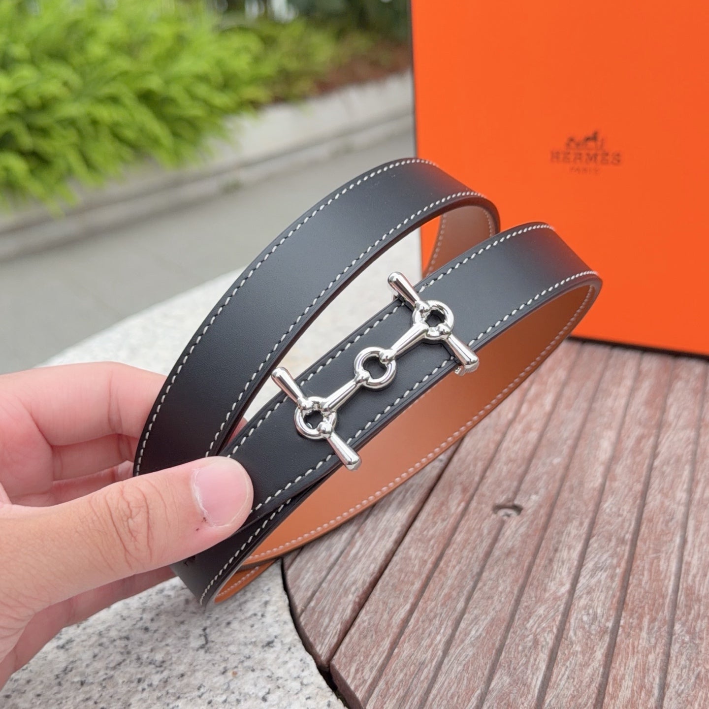 Hermes belt close-up: dark strap with tan underside and silver bit-style buckle.