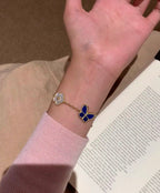 Gold-tone bracelet on wrist with blue butterfly and white clover charm links
