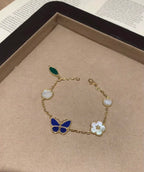 Gold-tone bracelet with blue butterfly, white clover charms, and green leaf accent
