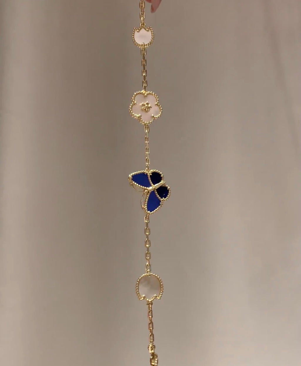 Gold-tone drop bracelet with blue butterfly, white clover, and round medallion charm