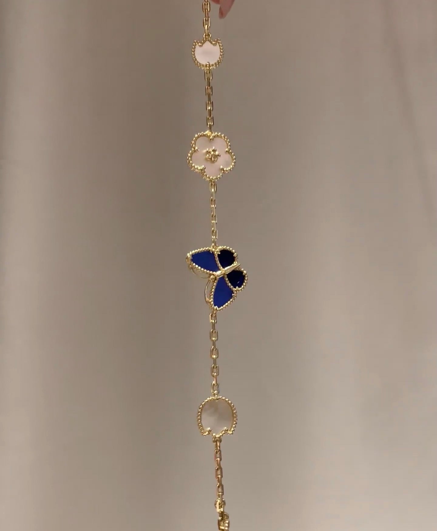 Gold-tone drop bracelet with blue butterfly, white clover, and round medallion charm