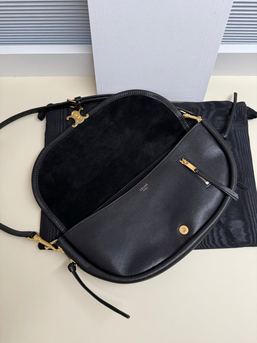 Black Celine crossbody bag with curved flap, gold hardware, and black strap