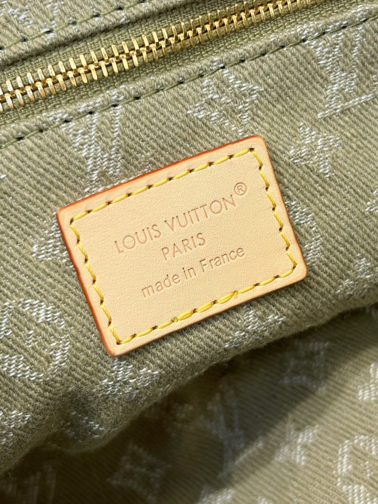 Louis Vuitton Paris label patch on olive-gray monogram canvas with tan border stitching.