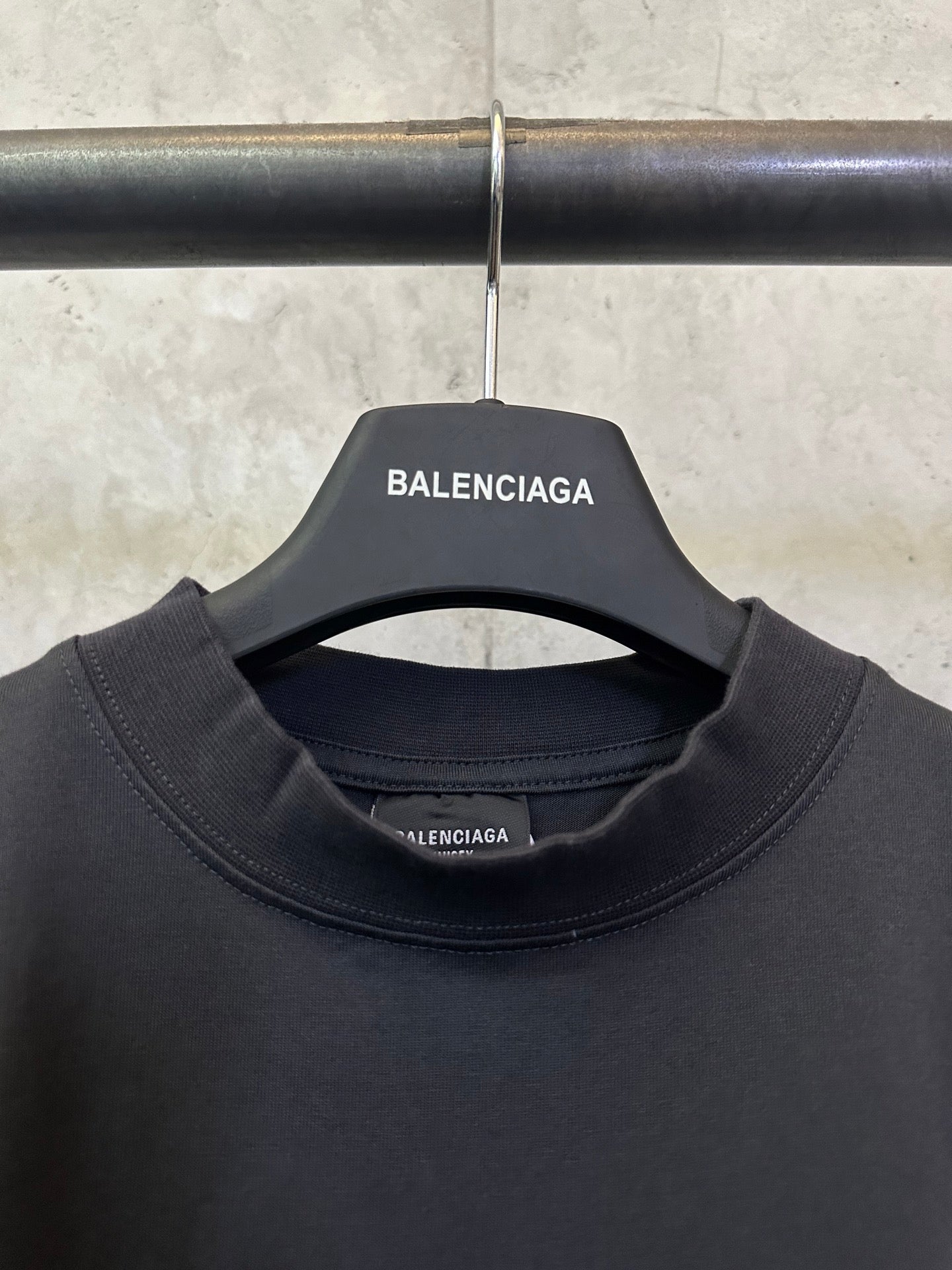 Neckline close-up of dark sleeveless top on hanger, with BALENCIAGA brand patch