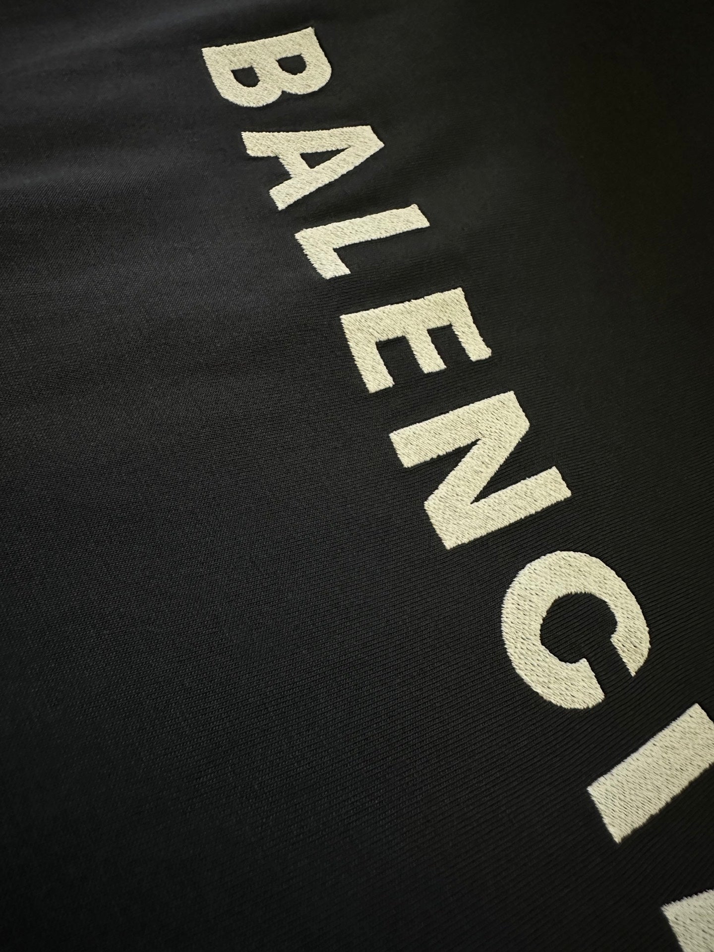 Close-up of dark sleeveless top with large beige BALENCIAGA text lettering